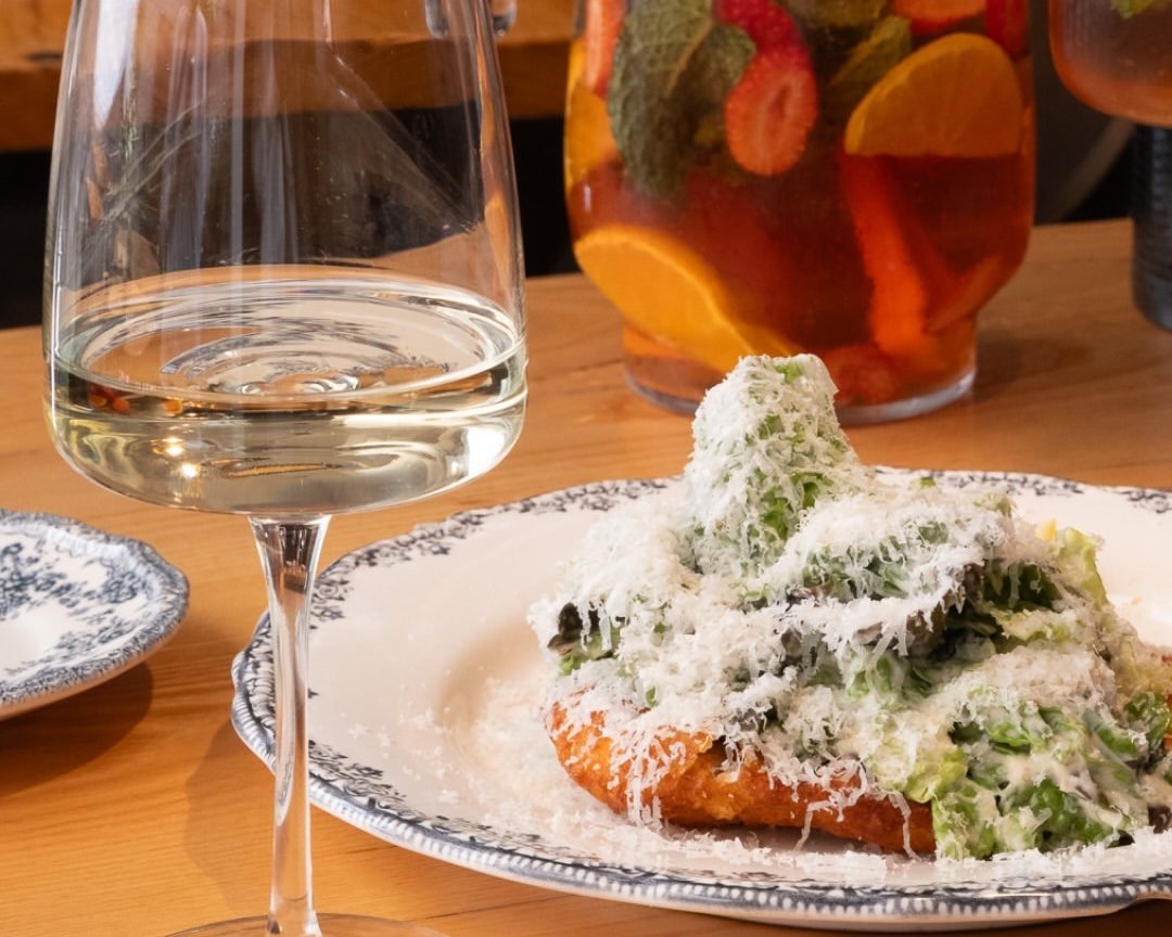 Escalope com salada e queijo ralado num prato azul e branco, ao lado de um copo de vinho branco