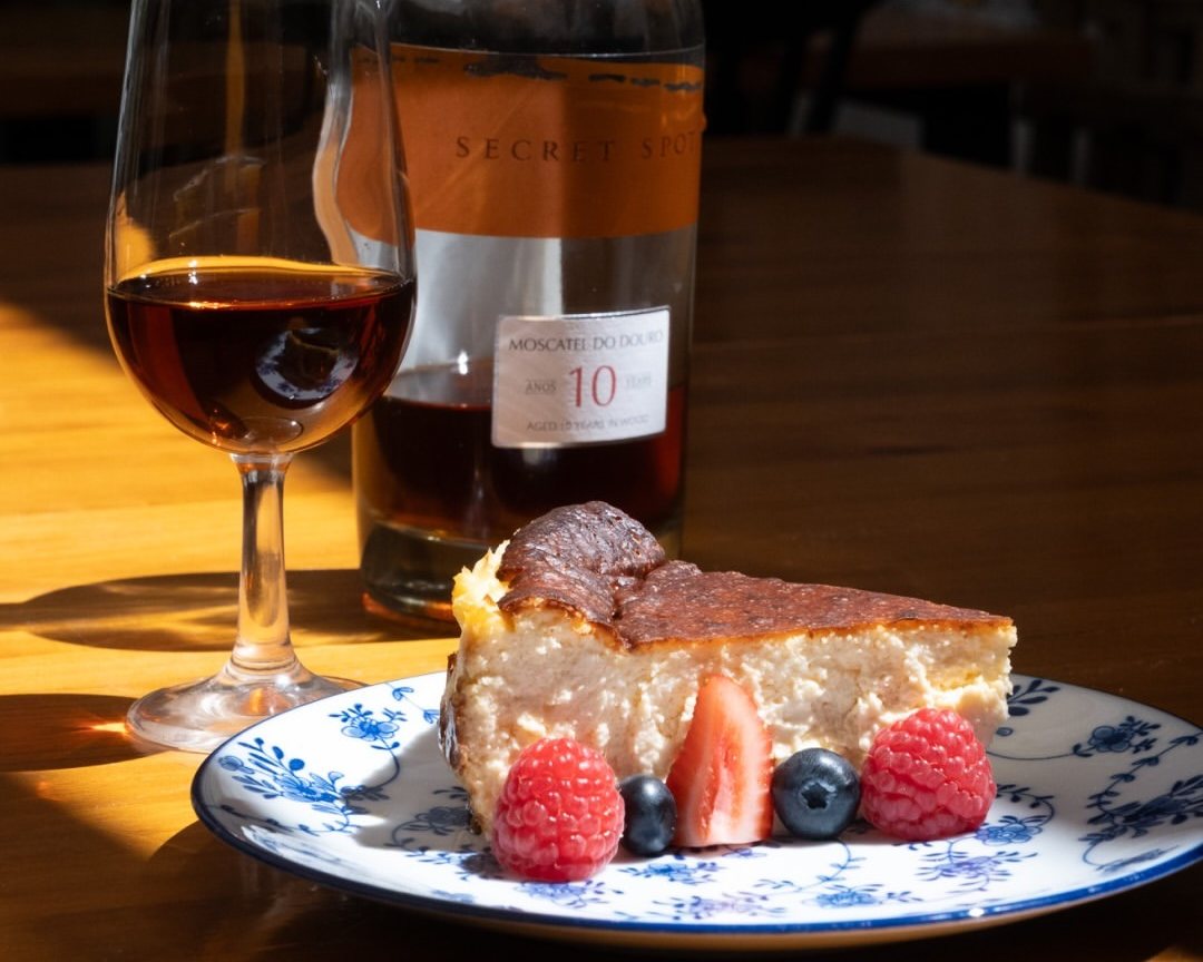 Fatia de sobremesa com frutos vermelhos num prato azul e branco, com um copo de vinho do Porto